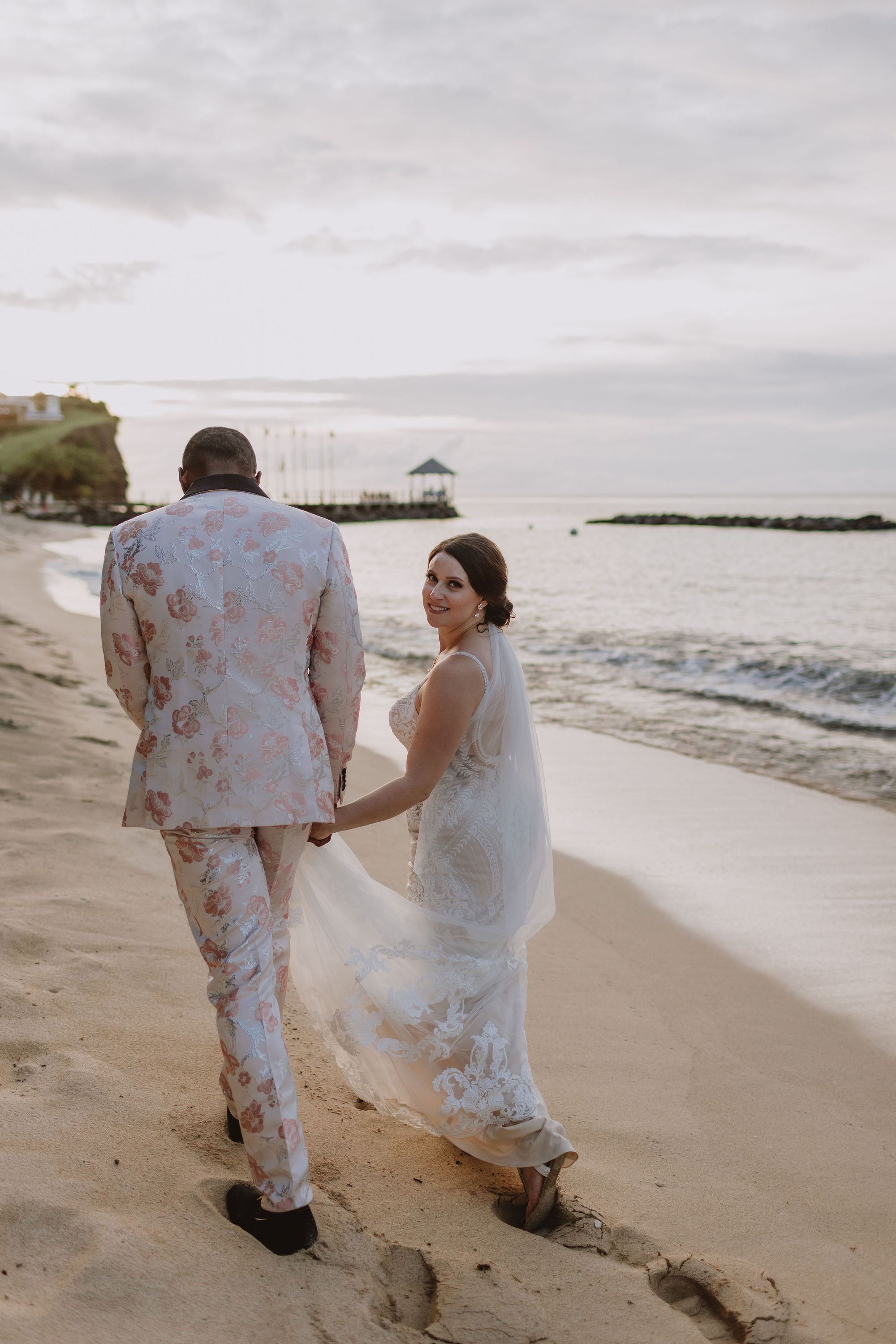bride and groom holding hands walking on shore and bride looking back