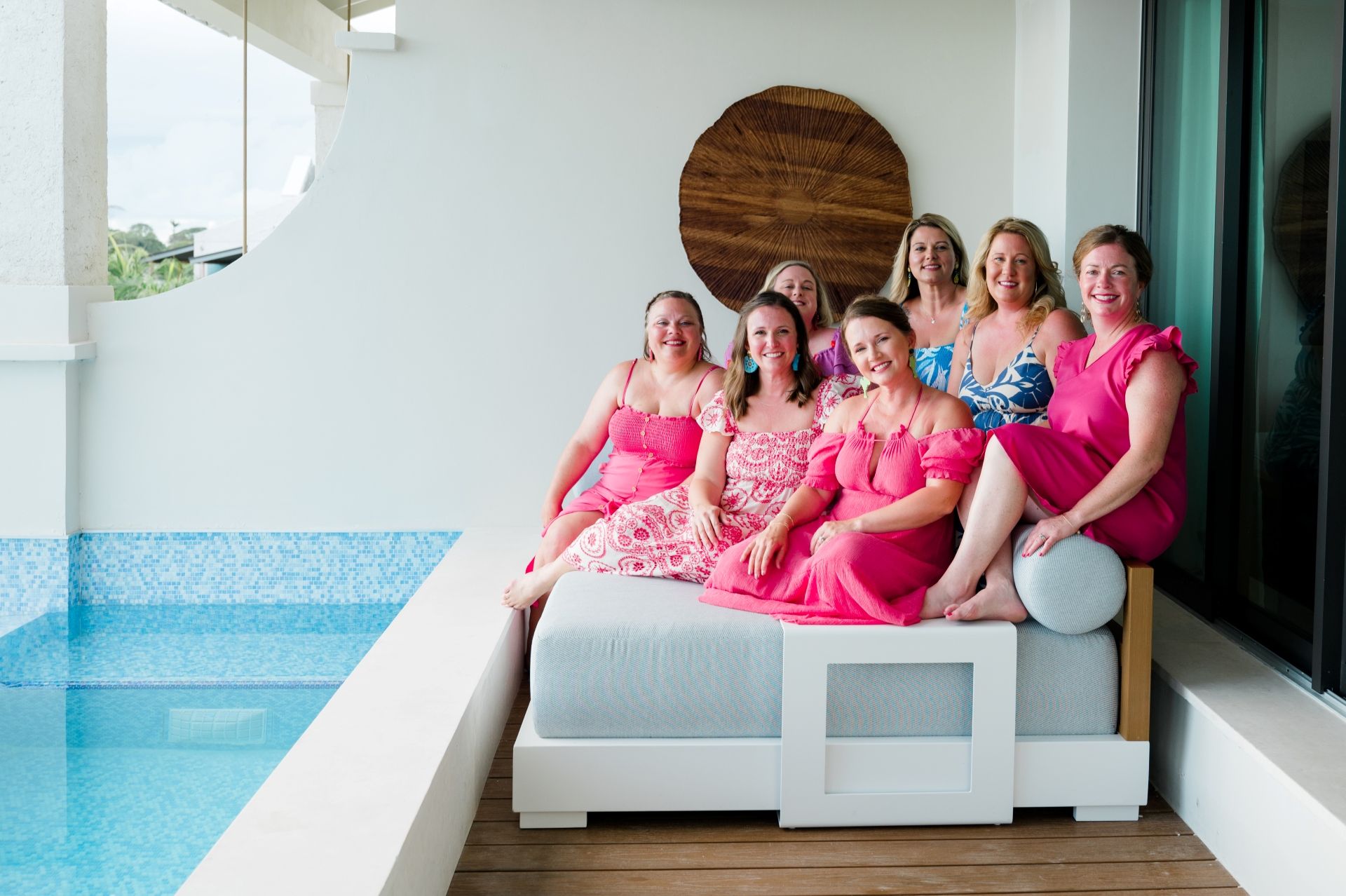 Group of women in pink and tropical dresses relaxing by a private suite pool