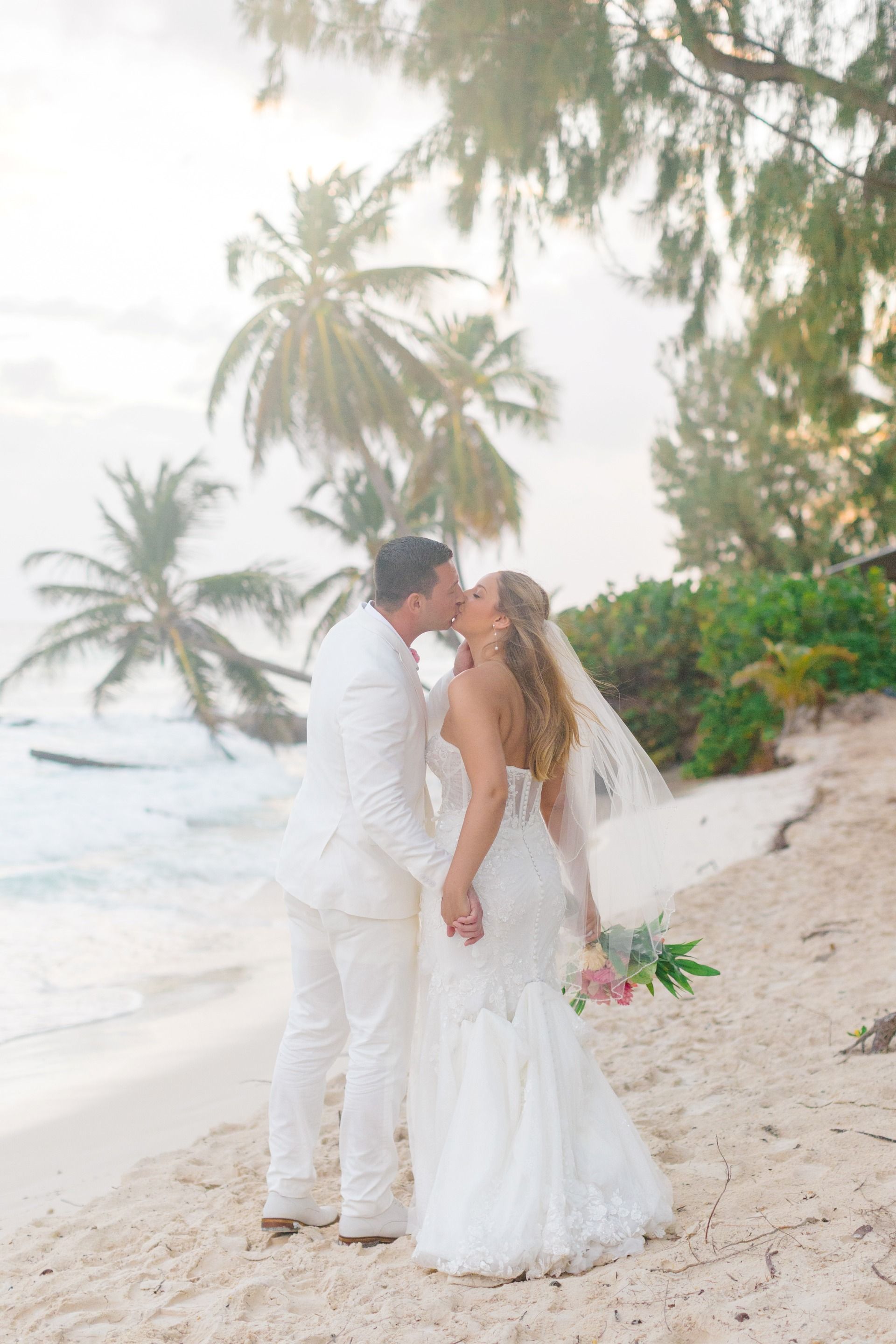 Bride and groom kissing on a Caribbean beach at sunset during a destination wedding